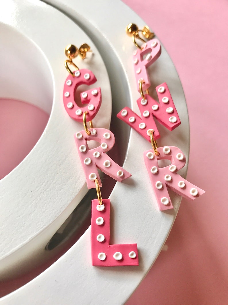 May include: Pink and white polka dot letter earrings spelling out "GIRL".