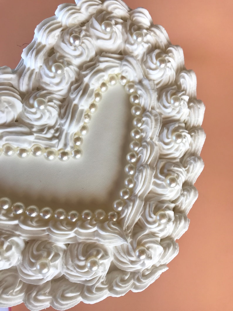 May include: White heart-shaped box with a raised, swirled design around the edges. The box is decorated with a border of white pearl beads.