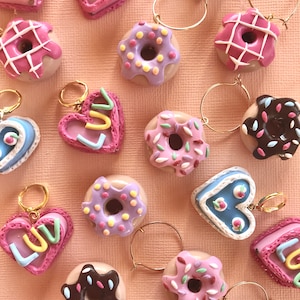 May include: A collection of colorful, handmade donut and heart-shaped charms with gold hoops. The donuts are decorated with sprinkles, icing, and chocolate. The hearts have the word "Luv" written on them.