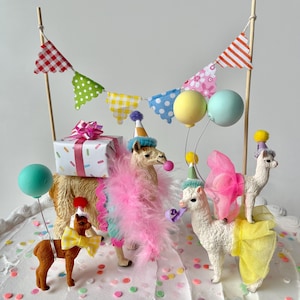K&ouml;nnte beinhalten: Festliche Tortendekoration mit Lama-Figuren, einem Pony und einer Geschenkbox. Die Lamas tragen Partyh&uuml;te, Federboas und Schleifen. Bunte Luftballons und ein Banner vervollst&auml;ndigen die festliche Szene.