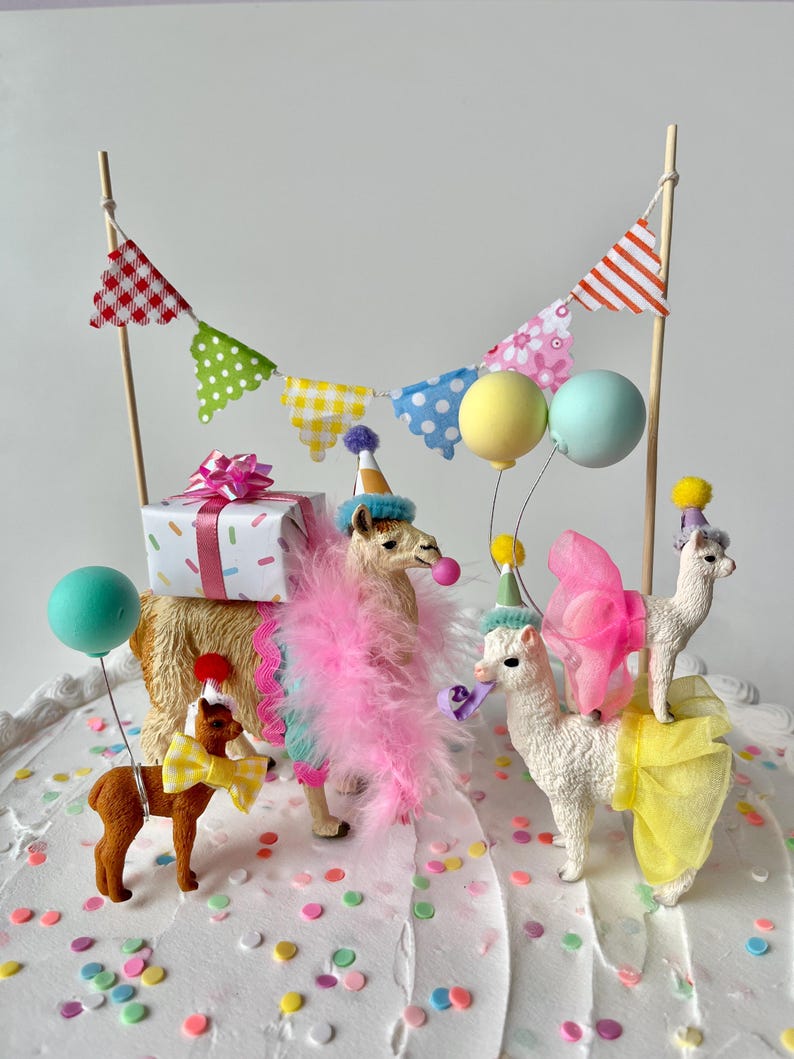 K&ouml;nnte beinhalten: Festliche Tortendekoration mit Lama-Figuren, einem Pony und einer Geschenkbox. Die Lamas tragen Partyh&uuml;te, Federboas und Schleifen. Bunte Luftballons und ein Banner vervollst&auml;ndigen die festliche Szene.