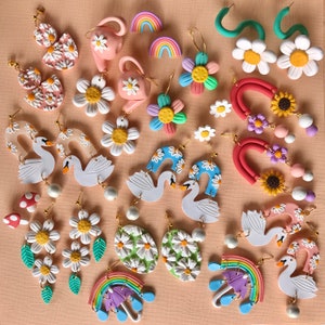 May include: Assortment of colorful polymer clay earrings featuring various designs, including flowers, swans, rainbows, and abstract shapes. The earrings are handmade and have a whimsical, playful aesthetic.