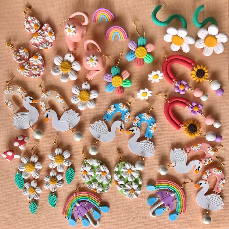 May include: Assortment of colorful polymer clay earrings featuring various designs, including flowers, swans, rainbows, and abstract shapes. The earrings are handmade and have a whimsical, playful aesthetic.
