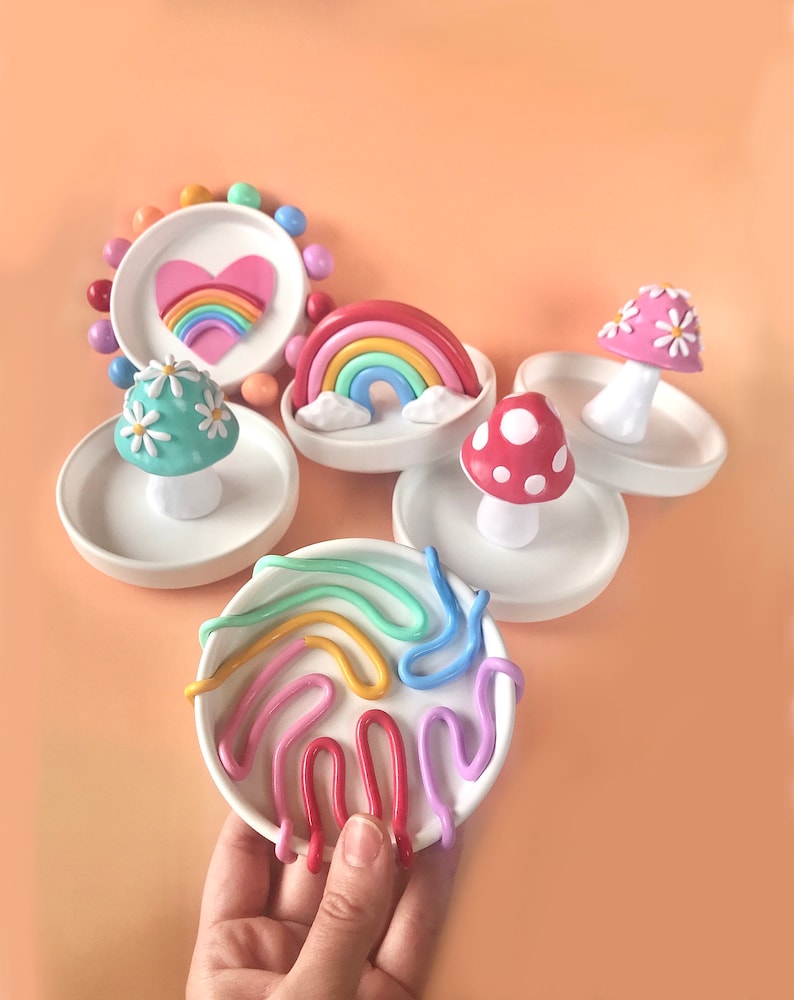 Puede incluir: Conjunto de cinco platos de anillos de cer&aacute;mica coloridos con un arco&iacute;ris, un coraz&oacute;n y hongos con lunares blancos y margaritas. Los platos son perfectos para guardar joyas u otros art&iacute;culos peque&ntilde;os.