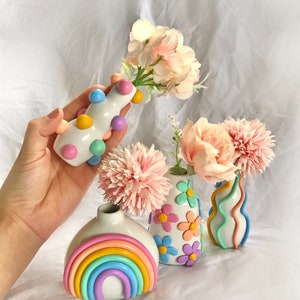 May include: Four handmade ceramic vases in pastel colors. One vase is decorated with a rainbow, another with flowers, another with wavy lines, and the last with colorful dots.