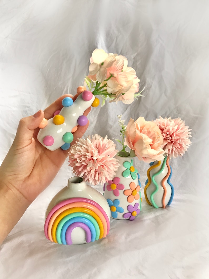 May include: Four handmade ceramic vases in pastel colors. One vase is decorated with a rainbow, another with flowers, another with wavy lines, and the last with colorful dots.