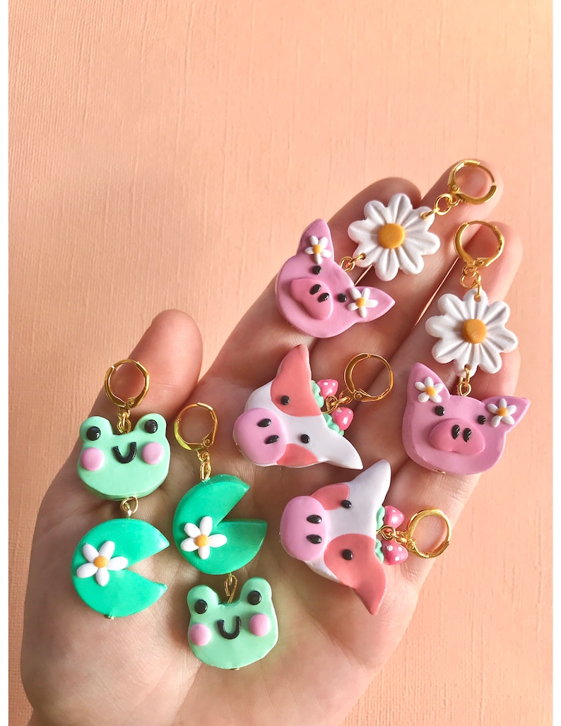 Pu&ograve; includere: Un set di sei paia di orecchini pendenti con vari disegni di animali e fiori. Gli orecchini sono realizzati in pasta polimerica e presentano una rana verde, un maiale rosa, una mucca con una corona di fragole, una margherita e una ninfea verde.