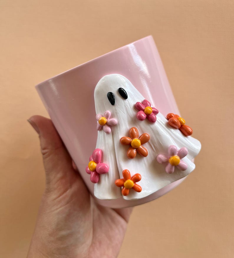 May include: A pink ceramic planter with a white ghost figurine decorated with pink, orange, and yellow flowers.