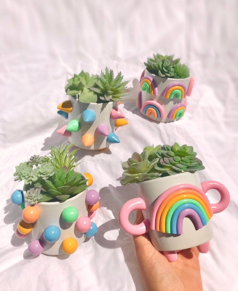 May include: Four colorful ceramic planters with succulents. The planters are decorated with rainbow designs, spikes, and colorful dots.
