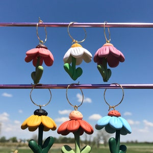 May include: Six pairs of flower-shaped earrings with gold hoops. The flowers are made of polymer clay and come in a variety of colors, including pink, white, yellow, orange, and blue.