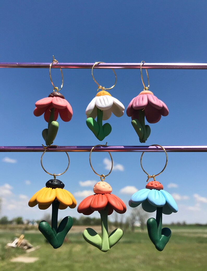 May include: Six pairs of flower-shaped earrings with gold hoops. The flowers are made of polymer clay and come in a variety of colors, including pink, white, yellow, orange, and blue.