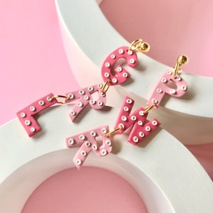 May include: Pink and white letter earrings with white polka dots. The letters are G, R, and P.