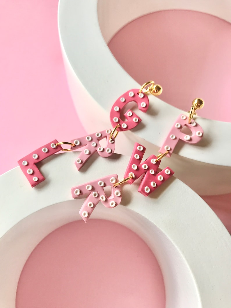 May include: Pink and white letter earrings with white polka dots. The letters are G, R, and P.