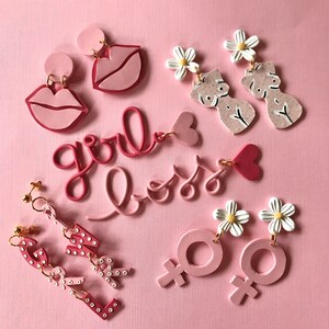 May include: Pink polymer clay earrings with various designs, including lips, flowers, female symbols, and the words "girl boss".