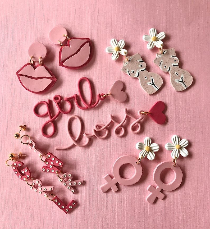 May include: Pink polymer clay earrings with various designs, including lips, flowers, female symbols, and the words "girl boss".
