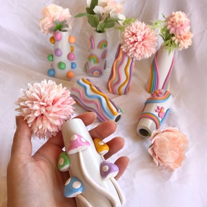 May include: Six small ceramic vases with different pastel colored designs. The vases are decorated with rainbows, wavy lines, polka dots, and mushrooms. The vases are perfect for holding small bouquets of flowers.
