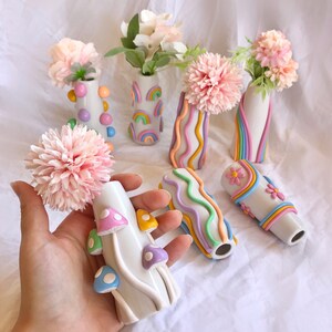 May include: A set of seven small ceramic vases with different pastel-colored designs. The vases are decorated with rainbows, wavy lines, dots, and mushrooms. The vases are perfect for displaying small bouquets of flowers.