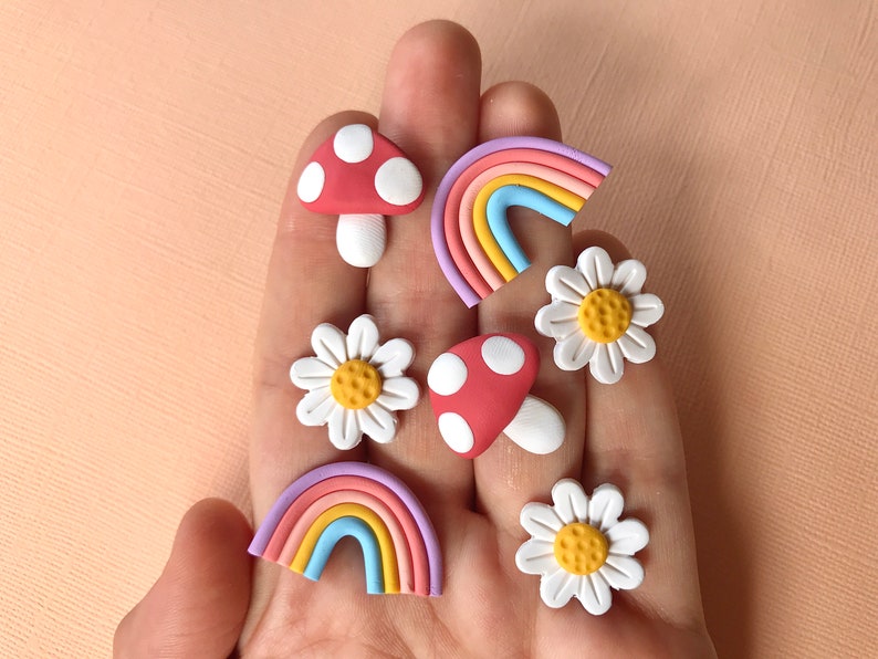 May include: A set of six colorful clay earrings featuring a rainbow, mushroom, and daisy designs. The earrings are handmade and have a whimsical, retro aesthetic.