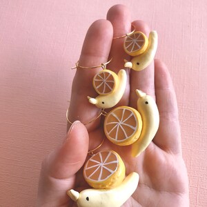 Pu&ograve; includere: Quattro paia di orecchini con una banana gialla sormontata da una fetta di limone. Gli orecchini sono realizzati in pasta polimerica e hanno cerchi dorati.
