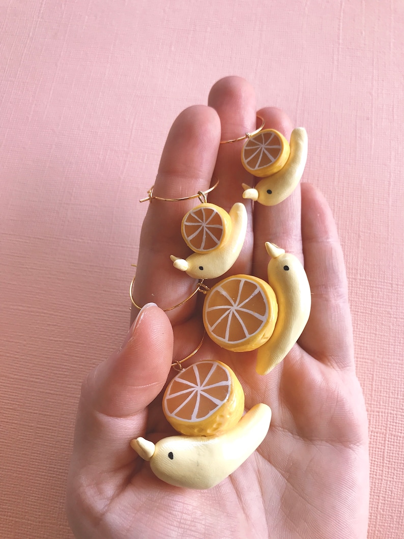 Pu&ograve; includere: Quattro paia di orecchini con una banana gialla sormontata da una fetta di limone. Gli orecchini sono realizzati in pasta polimerica e hanno cerchi dorati.