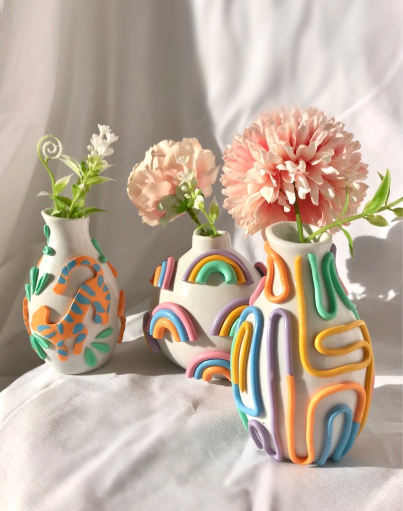 May include: Three ceramic vases with different designs. The vase on the left has a blue and orange pattern. The middle vase has a rainbow pattern. The vase on the right has a multi-colored pattern of lines and curves.