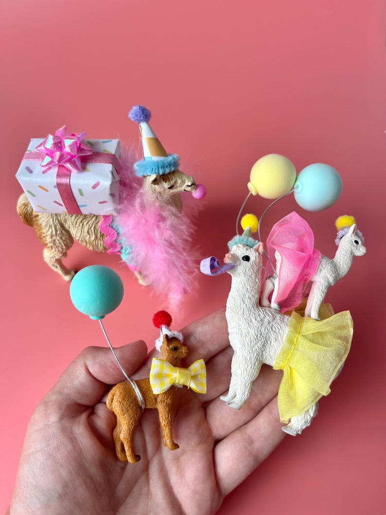K&ouml;nnte beinhalten: Eine Sammlung skurriler Lama-Figuren, jede mit festlicher Partykleidung. Ein Lama tr&auml;gt ein Geschenk, andere tragen Partyh&uuml;te, Federboas und Luftballons. Die Figuren sind vor einem einfarbigen rosa Hintergrund platziert.