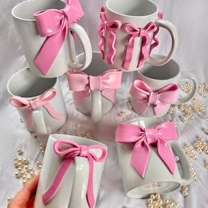 Pu&ograve; includere: Set di sei tazze in ceramica bianca con fiocchi rosa. I fiocchi sono realizzati in un materiale morbido e flessibile e sono fissati alle tazze con un adesivo resistente. Le tazze sono perfette per aggiungere un tocco di fantasia a qualsiasi cucina o ufficio.