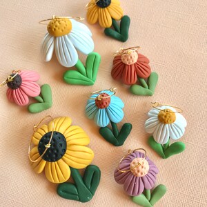 May include: Eight pairs of polymer clay flower earrings with gold hoops. The flowers are in various colors, including white, yellow, blue, purple, pink, and orange.