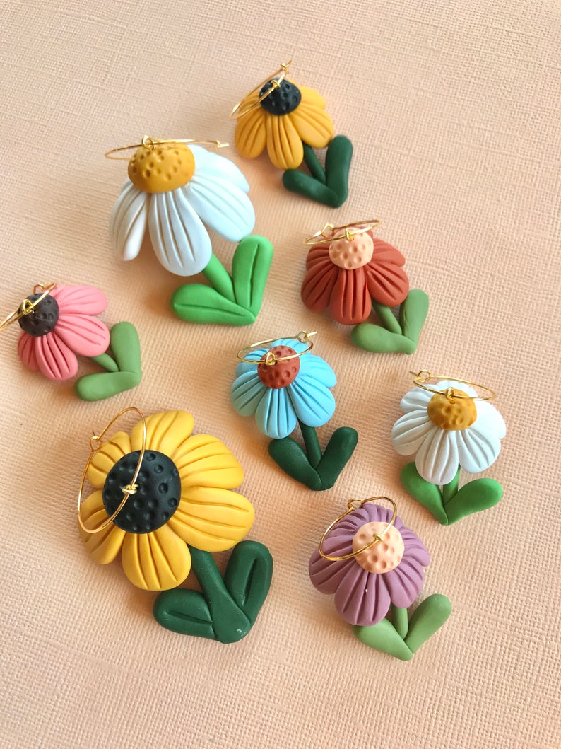 May include: Eight pairs of polymer clay flower earrings with gold hoops. The flowers are in various colors, including white, yellow, blue, purple, pink, and orange.