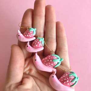 Pu&ograve; includere: Quattro ciondoli a forma di lumaca rosa con pois bianchi e foglie verdi che portano ciondoli a forma di fragola rosa e bianca.