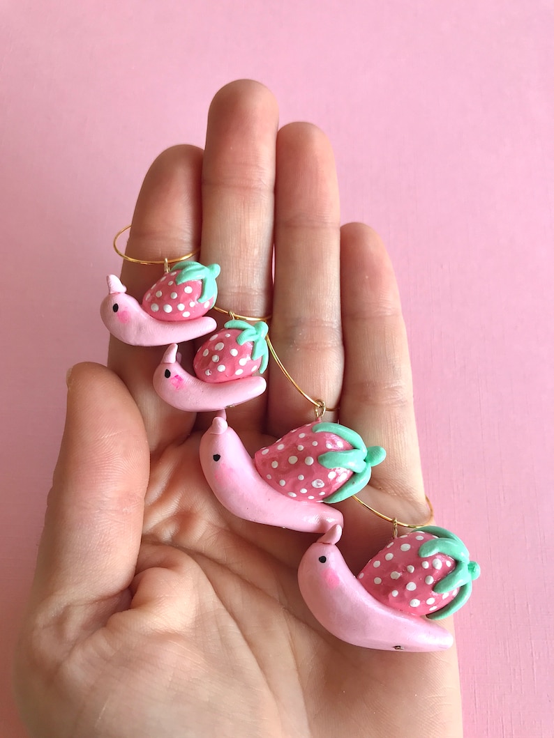 Pu&ograve; includere: Quattro ciondoli a forma di lumaca rosa con pois bianchi e foglie verdi che portano ciondoli a forma di fragola rosa e bianca.
