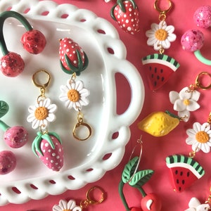 May include: A collection of colorful fruit-themed charms, including cherries, strawberries, watermelons, lemons, and daisies. The charms are made of polymer clay and have a whimsical, handmade aesthetic. They are perfect for adding a touch of summer fun to jewelry, bags, or keychains.