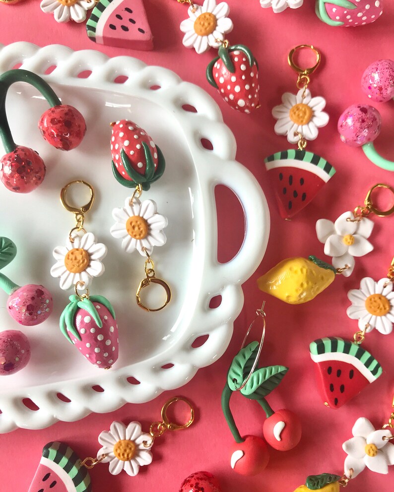 May include: A collection of colorful fruit-themed charms, including cherries, strawberries, watermelons, lemons, and daisies. The charms are made of polymer clay and have a whimsical, handmade aesthetic. They are perfect for adding a touch of summer fun to jewelry, bags, or keychains.