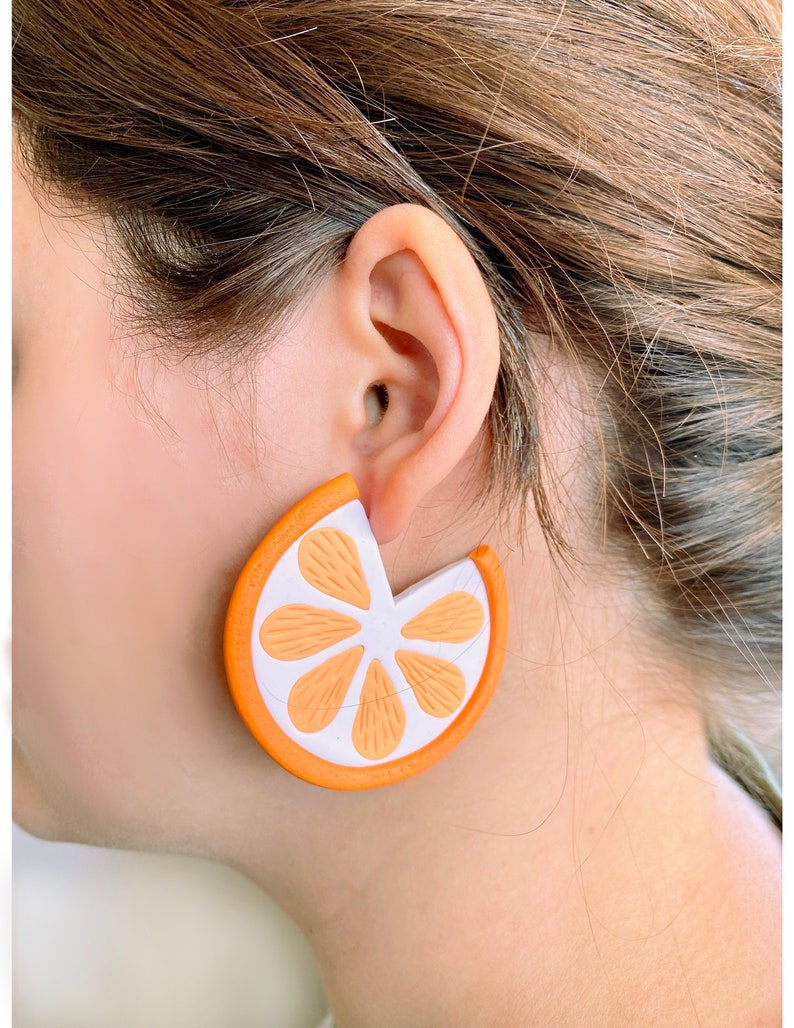 May include: Orange slice shaped earrings with a white center and orange edges. The earrings are made of a lightweight material and are perfect for adding a touch of whimsy to any outfit.