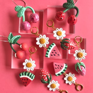 May include: A set of colorful polymer clay earrings featuring watermelon, strawberry, daisy, and cherry designs. The earrings are handmade and have gold-toned hooks.