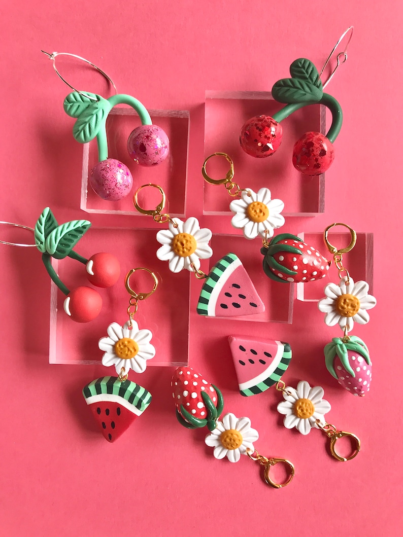 May include: A set of colorful polymer clay earrings featuring watermelon, strawberry, daisy, and cherry designs. The earrings are handmade and have gold-toned hooks.