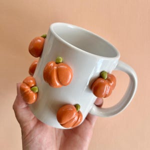 May include: White ceramic mug with orange and green pumpkin decorations.