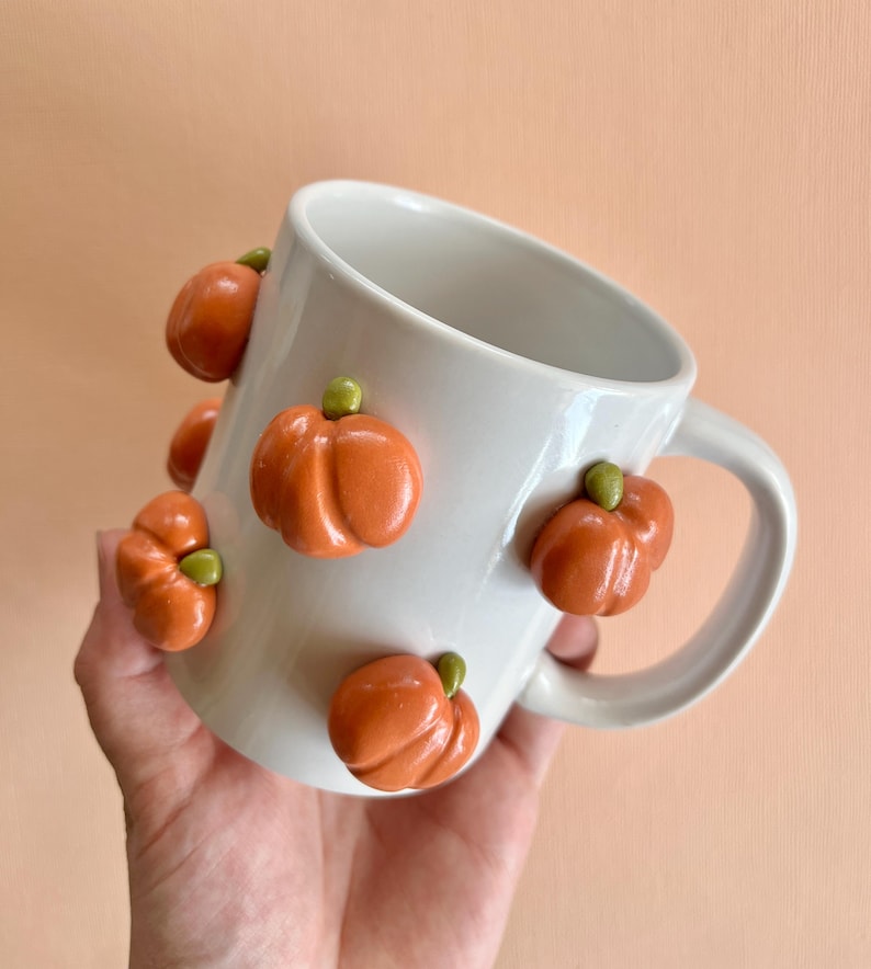 May include: White ceramic mug with orange and green pumpkin decorations.