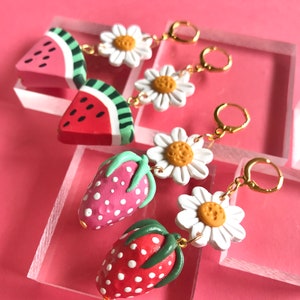 May include: Three pairs of handmade polymer clay earrings. The first pair features a watermelon slice and a white daisy. The second pair features a strawberry and a white daisy. The third pair features a strawberry and a white daisy.