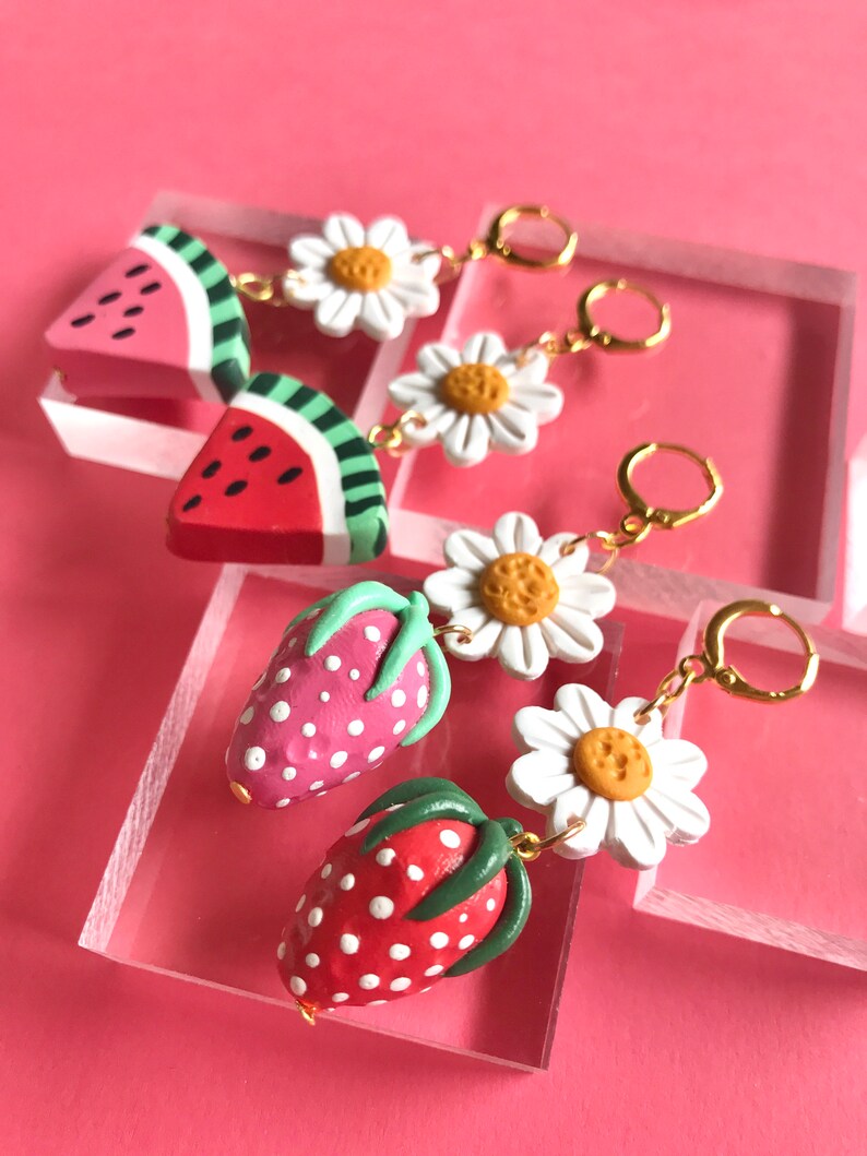 May include: Three pairs of handmade polymer clay earrings. The first pair features a watermelon slice and a white daisy. The second pair features a strawberry and a white daisy. The third pair features a strawberry and a white daisy.