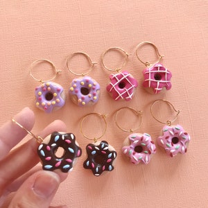 May include: Six pairs of donut earrings with gold hoops. The donuts are made of polymer clay and have different colored glazes and sprinkles. The donuts are pink, purple, and brown.