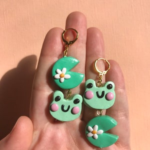 Pu&ograve; includere: Un paio di orecchini a forma di rana verde e Pac-Man verde con margherite bianche. Gli orecchini sono realizzati in pasta polimerica e hanno cerchi dorati.
