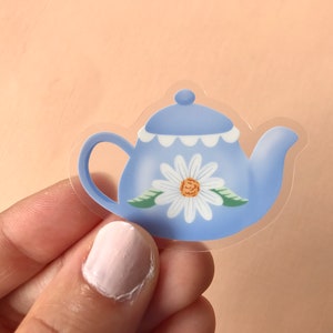May include: A blue teapot with a white daisy design and a scalloped rim. The teapot is made of clear vinyl and is perfect for adding a touch of whimsy to your craft projects.