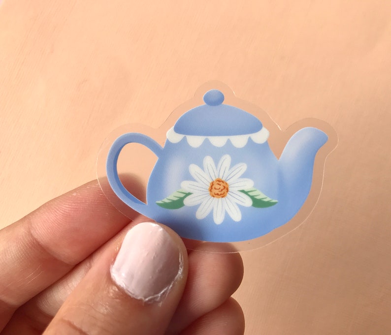 May include: A blue teapot with a white daisy design and a scalloped rim. The teapot is made of clear vinyl and is perfect for adding a touch of whimsy to your craft projects.