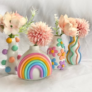 May include: Four ceramic vases with pastel rainbow and floral designs. The vases are filled with pink flowers.