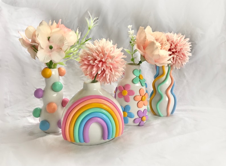 May include: Four ceramic vases with pastel rainbow and floral designs. The vases are filled with pink flowers.