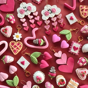 May include: Assortment of pink and white polymer clay earrings featuring various designs, including hearts, clouds, strawberries, cakes, and letters.