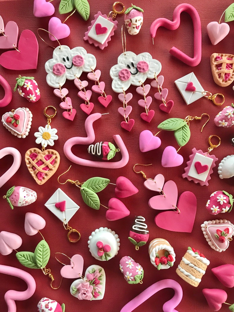 May include: Assortment of pink and white polymer clay earrings featuring various designs, including hearts, clouds, strawberries, cakes, and letters.