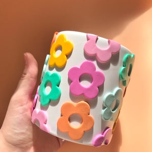May include: White ceramic planter with a colourful flower design. The flowers are in shades of pink, orange, yellow, and green.