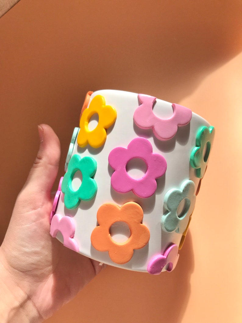 May include: White ceramic planter with a colourful flower design. The flowers are in shades of pink, orange, yellow, and green.